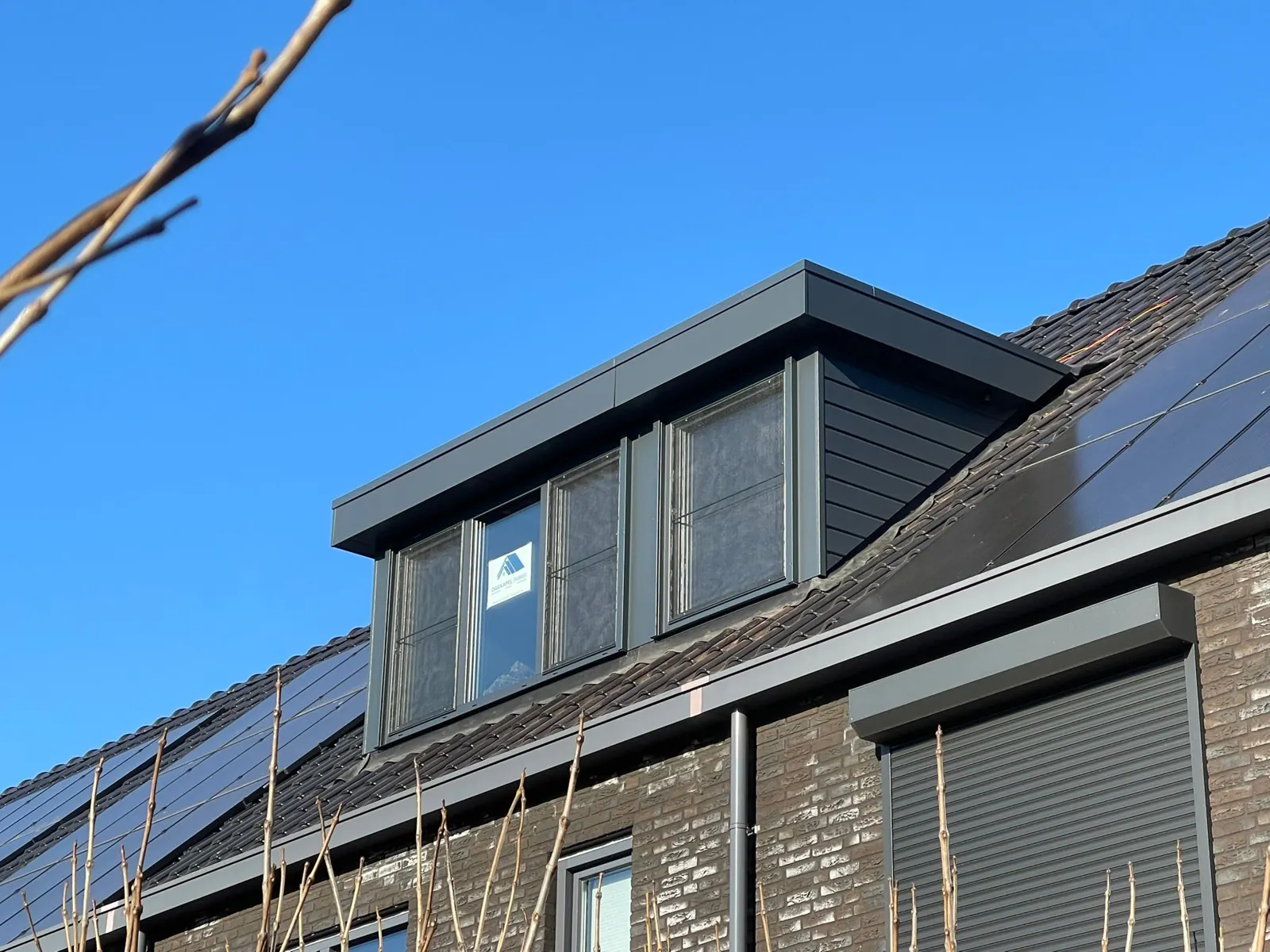 Antraciet dakkapel op een nieuwbouwwoning tussen zonnepanelen