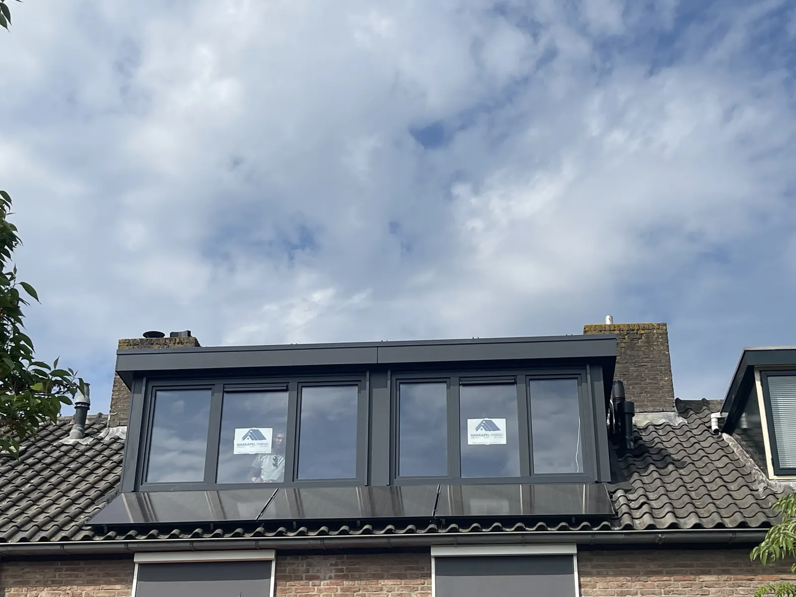 Antraciet dakkapel boven zonnepanelen op een rijwoning