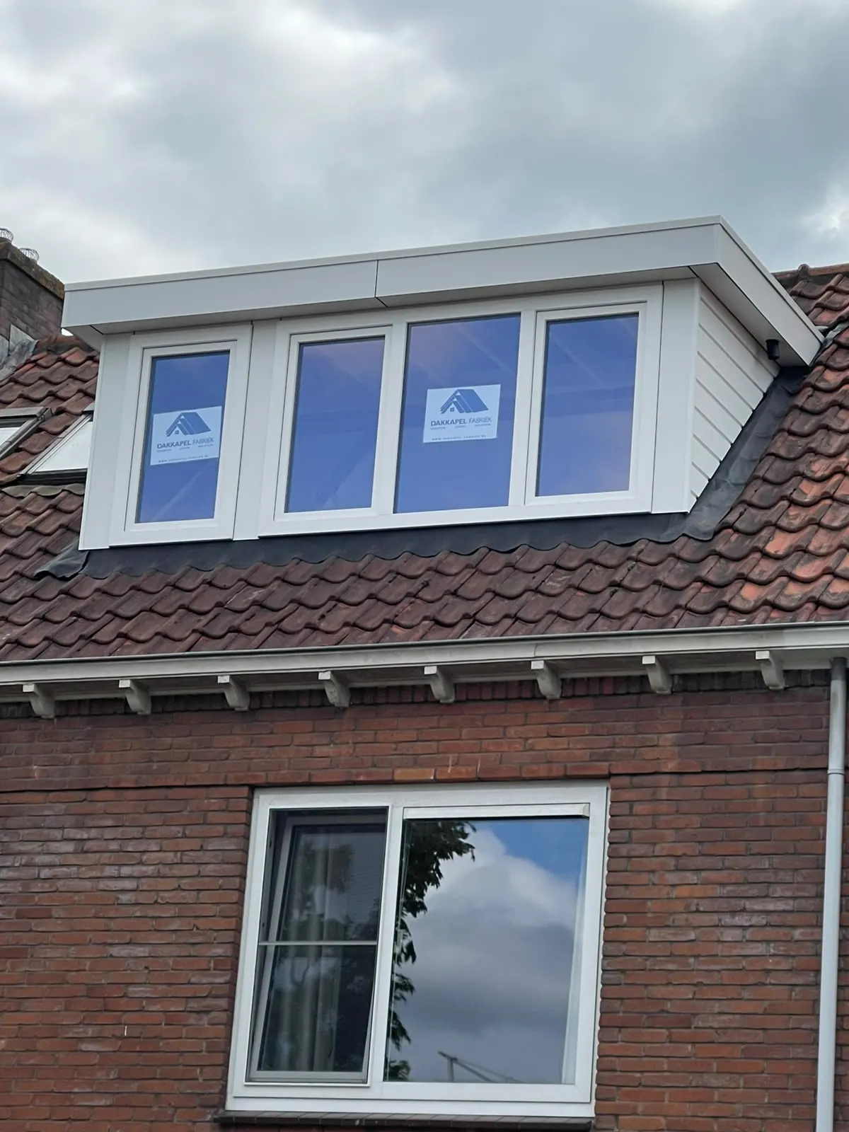 Witte dakkapel met vier ramen op een bakstenen woning