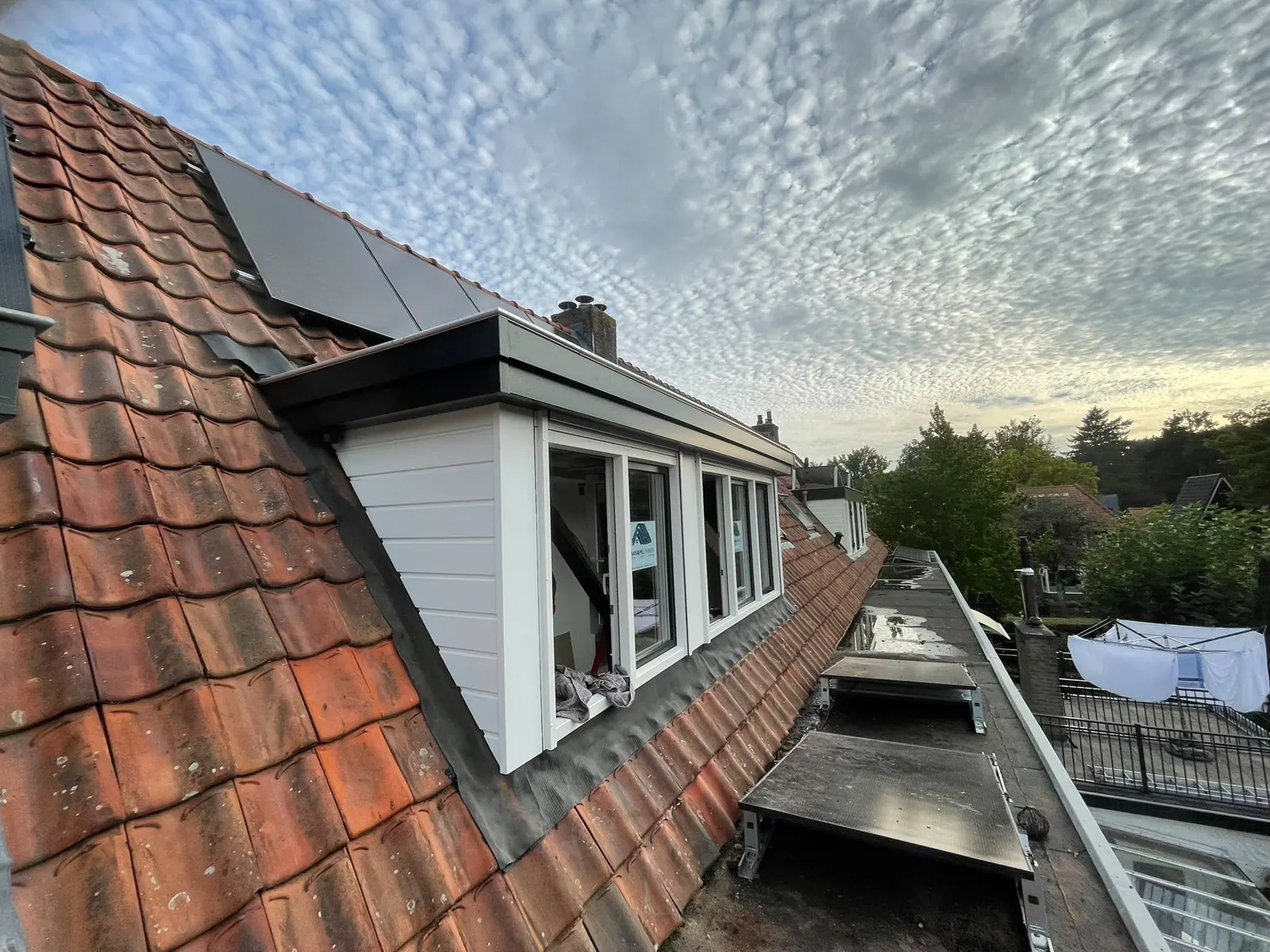 Dakkapel subsidie: witte dakkapel met rolluiken naast zonnepanelen